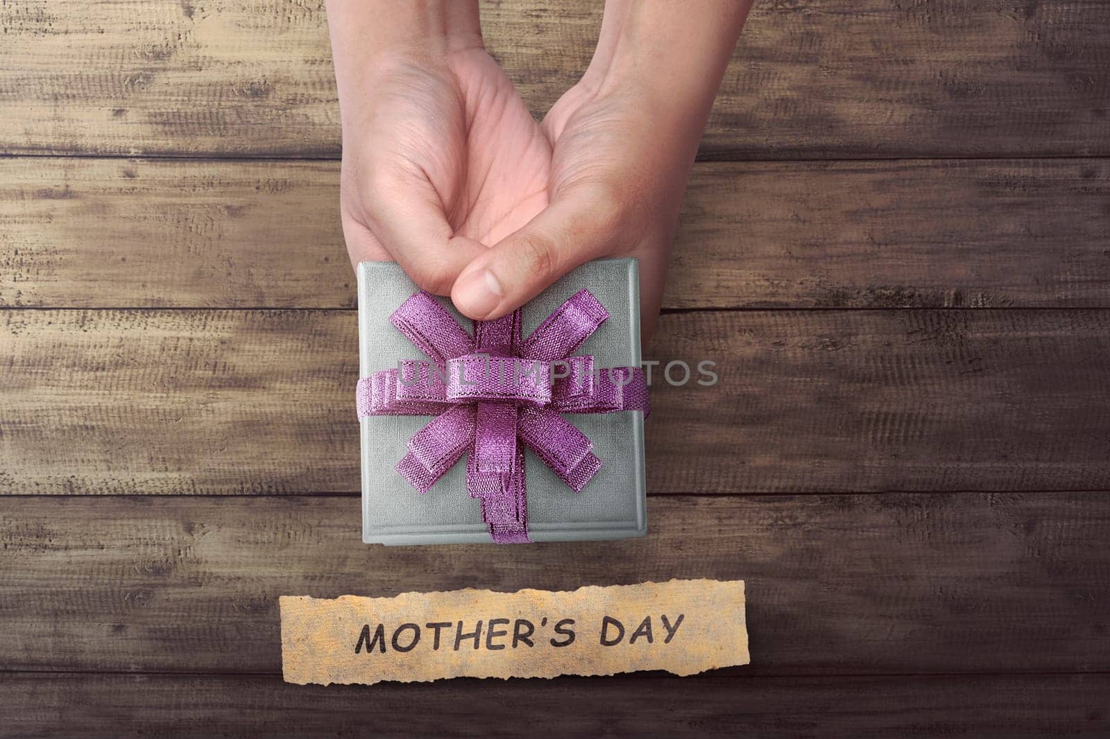 People hand holding small gift with Mother's Day greeting on wooden table