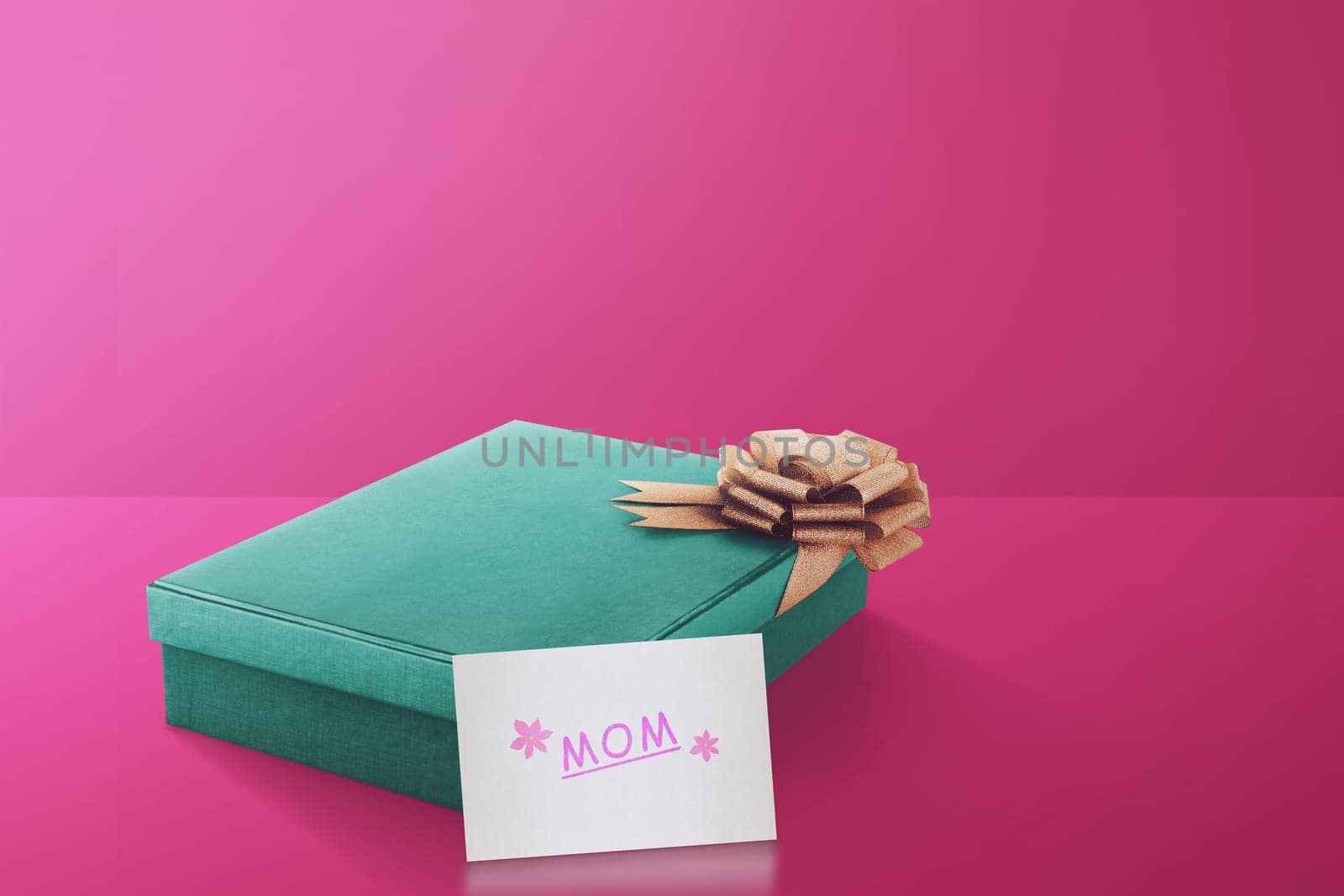 Gift box with gold ribbon and mom text on paper over pink background