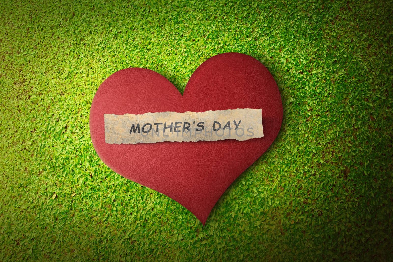 Mothers day message on paper in red heart over green grass background