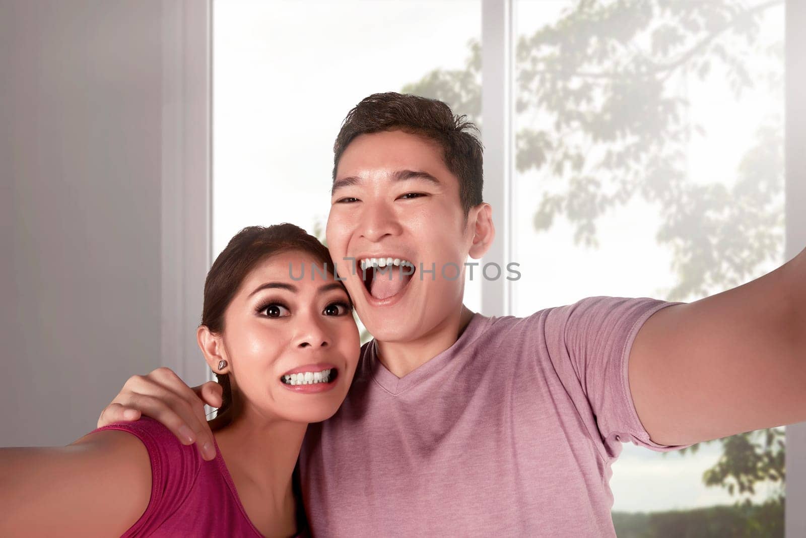 Young asian couple taking selfie photo with big windows interior in home