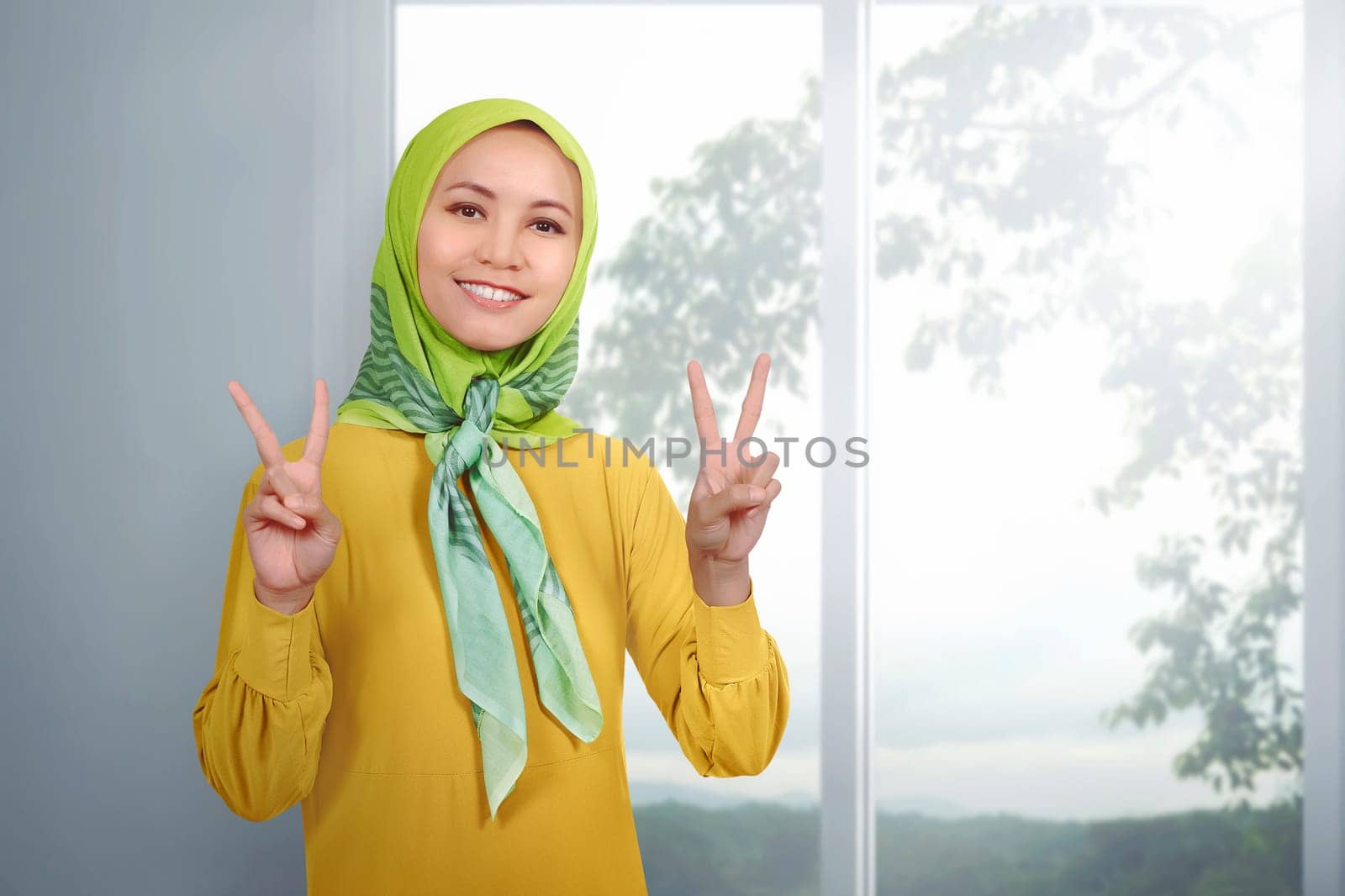 Young asian woman muslim giving peace sign against indoor background