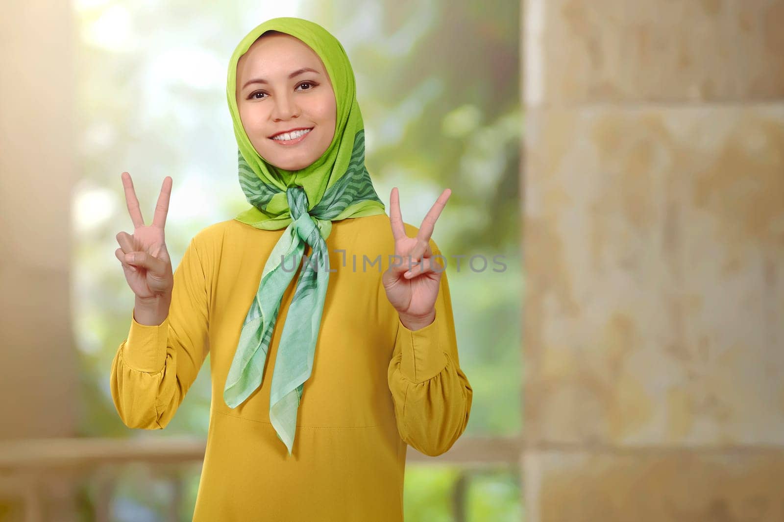 Smiling asian woman girl with hijab showing peace sign in the mosque