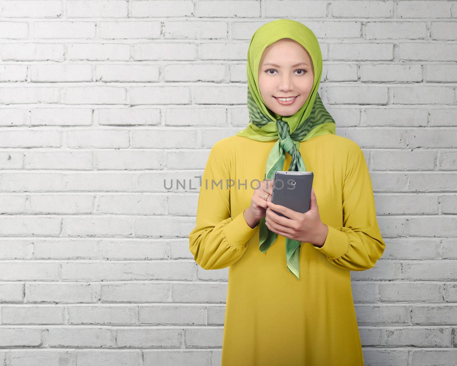 Asian muslim woman standing while using smartphone over white wall background