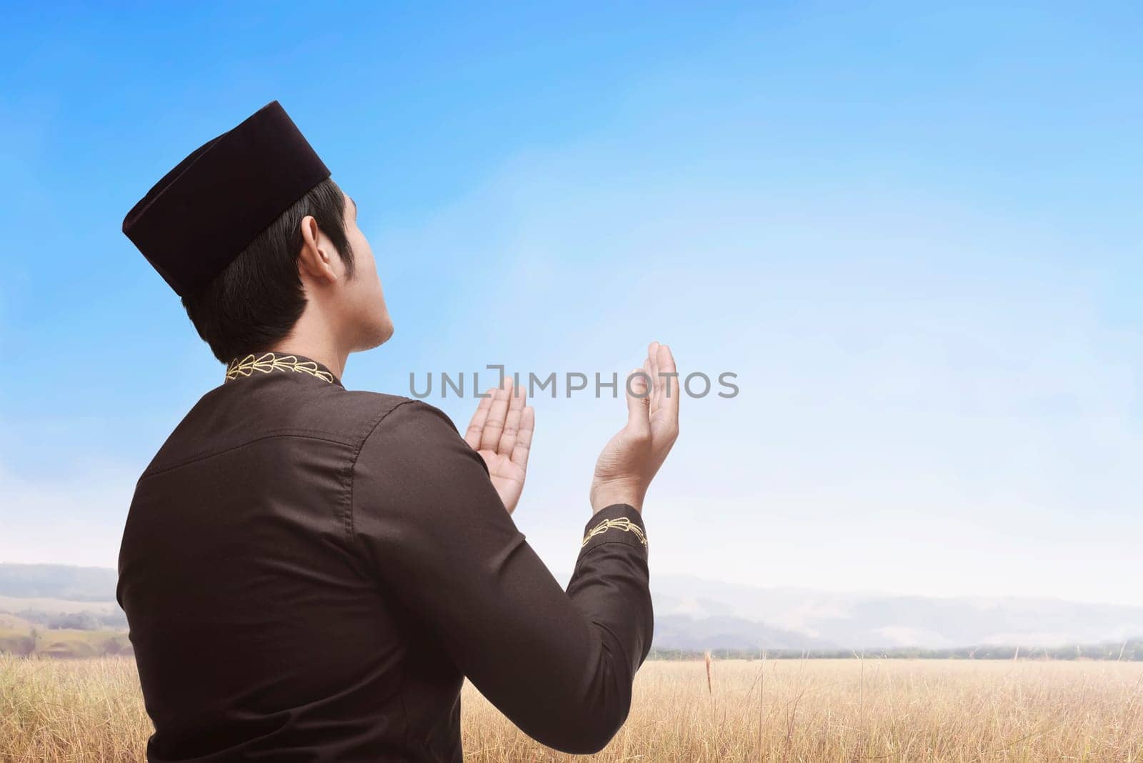Religious asian muslim man with black cap praying in the meadow field