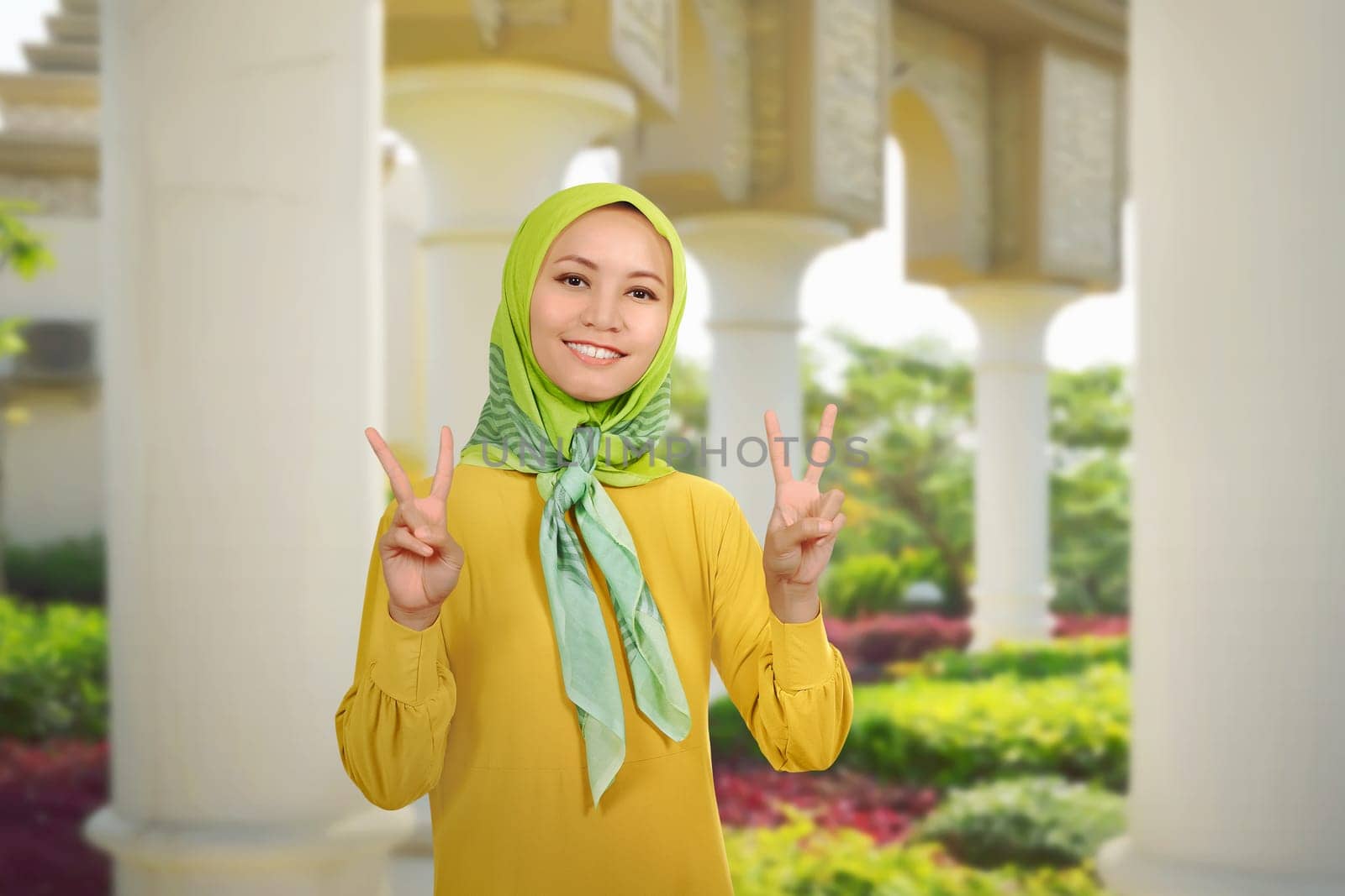 Beautiful asian muslim woman showing two fingers over against outdoor background
