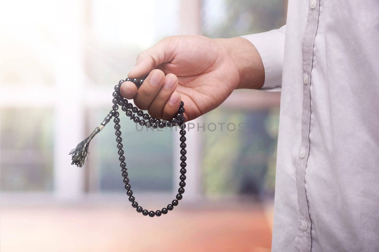Hand of muslim man praying while holding tasbih against blurred background