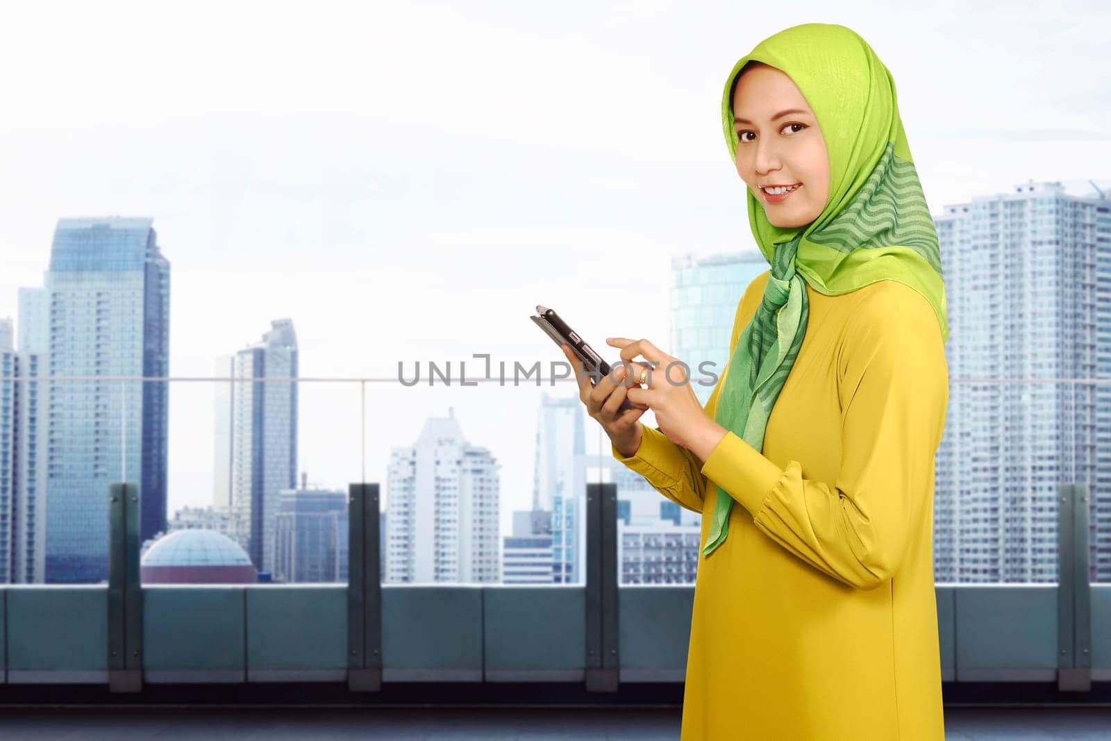Smiling asian muslim woman using a smartphone against skyscraper background