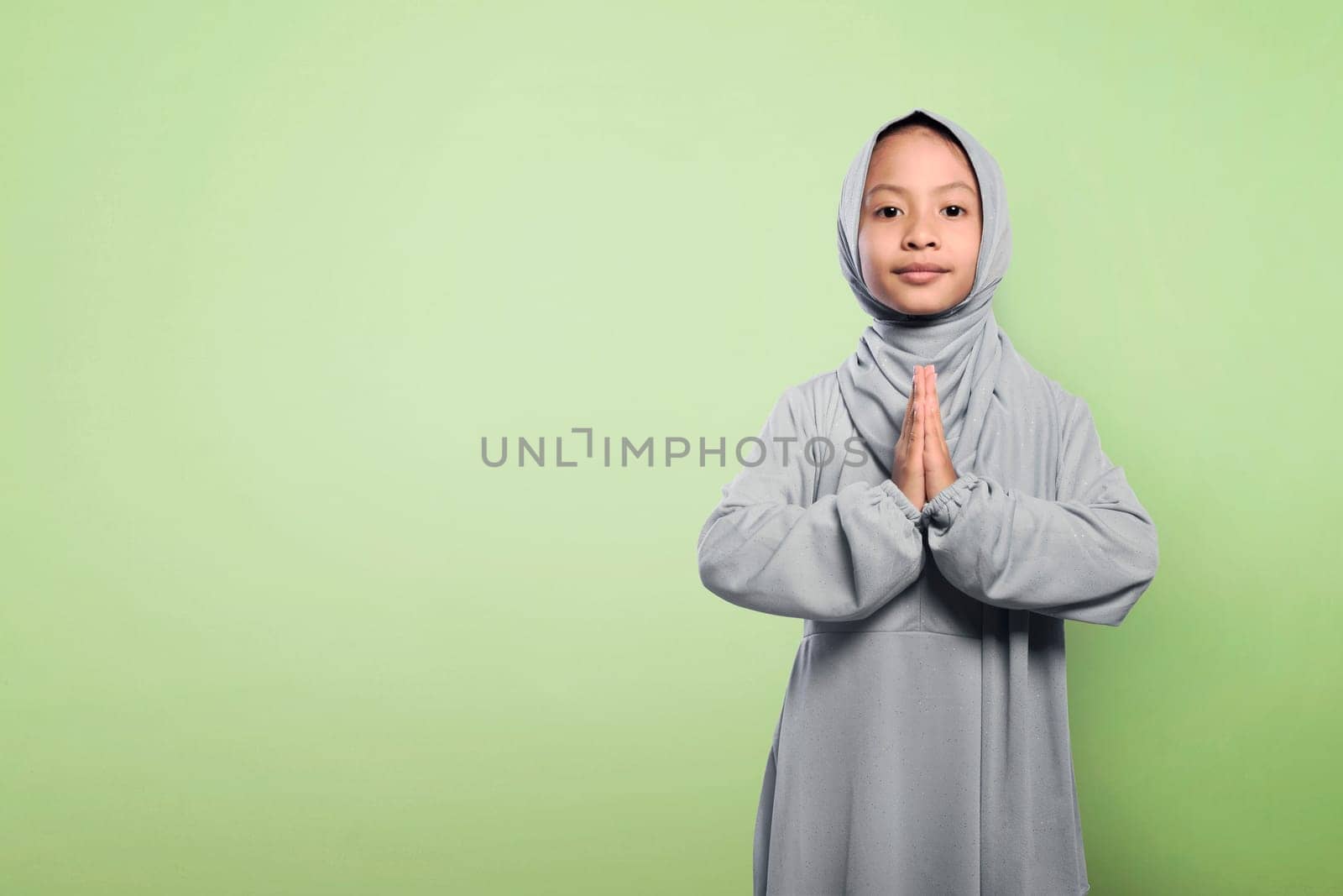 Little asian muslim girl in hijab clothes praying over green background