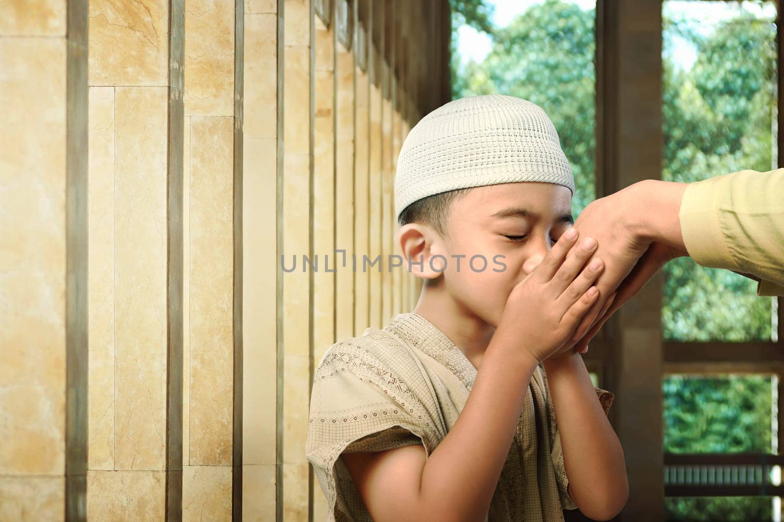 Asian muslim kid kissing his parent hand as respect symbol in the mosque