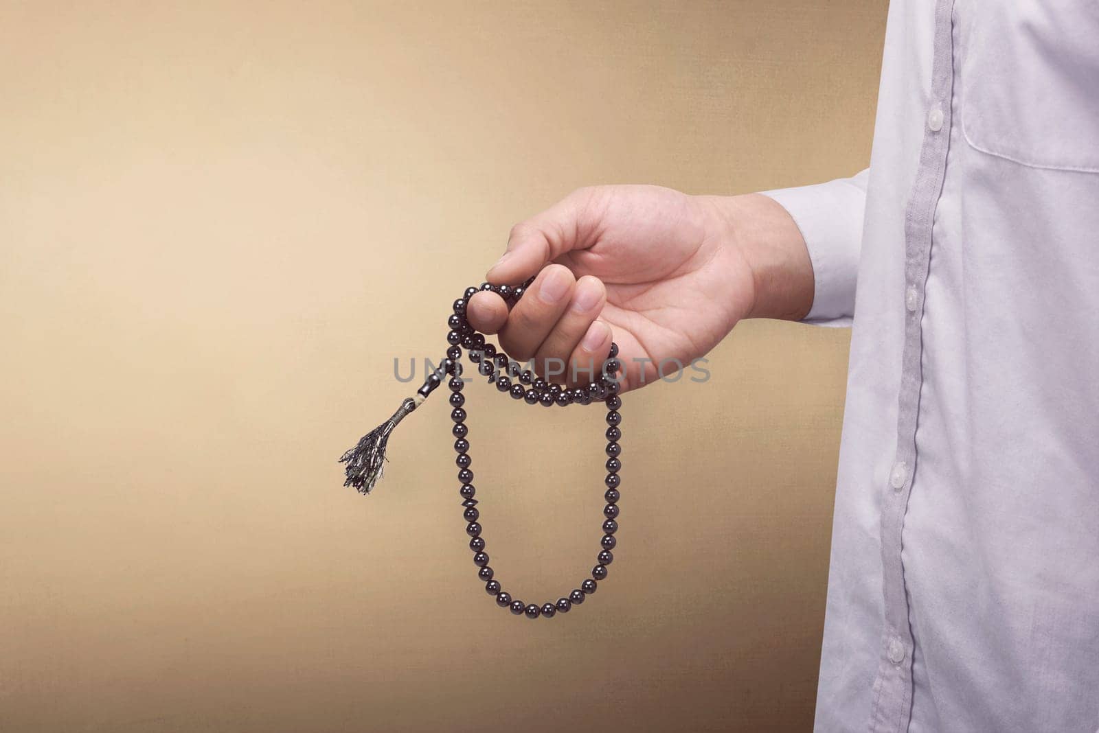 Hand of muslim man praying while holding tasbih over brown background