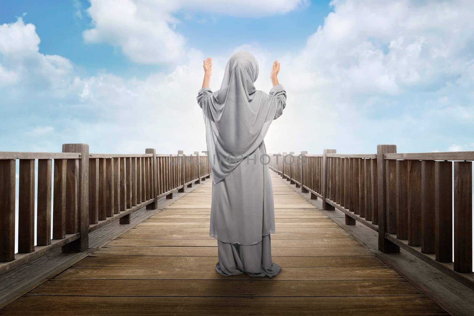 Back view of asian muslim girl standing and praying to god with blue sky background