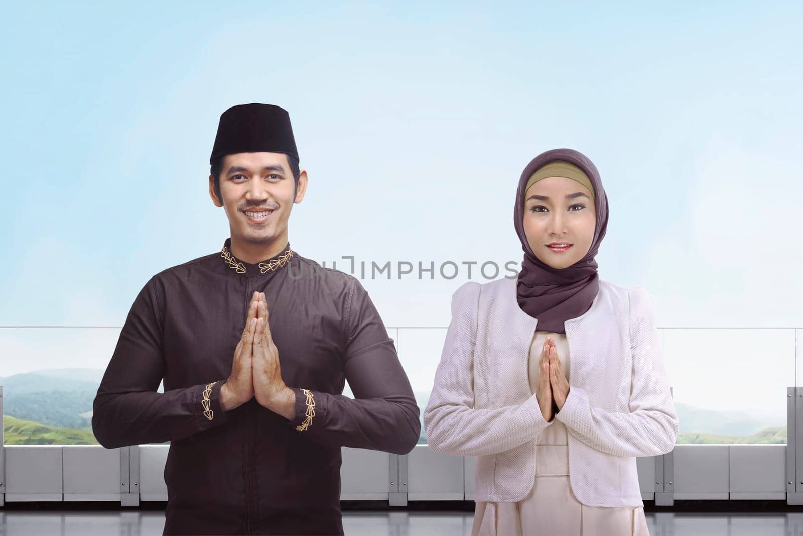 Asian muslim man and woman with traditional dress praying together against blue sky background