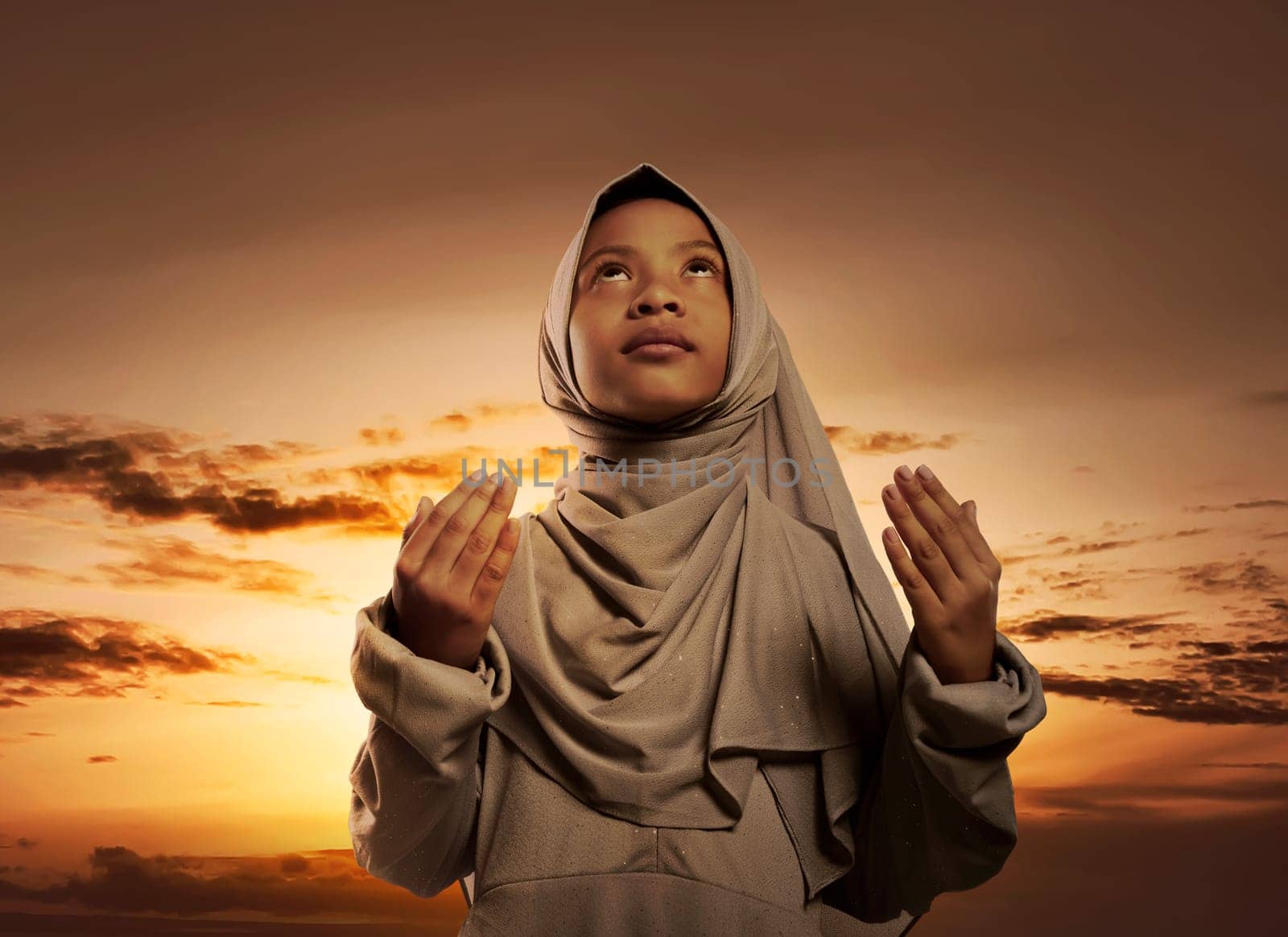 Little asian muslim girl with hijab praying to god over sunset background