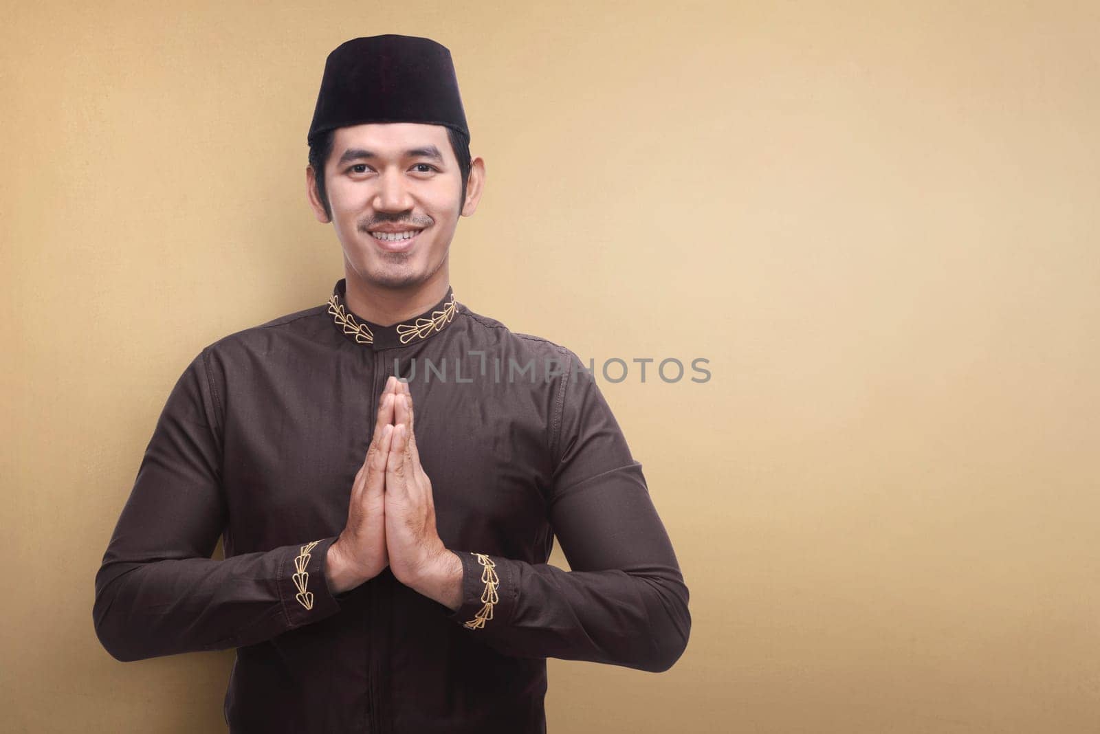 Handsome asian muslim man wearing traditional dress praying against brown background
