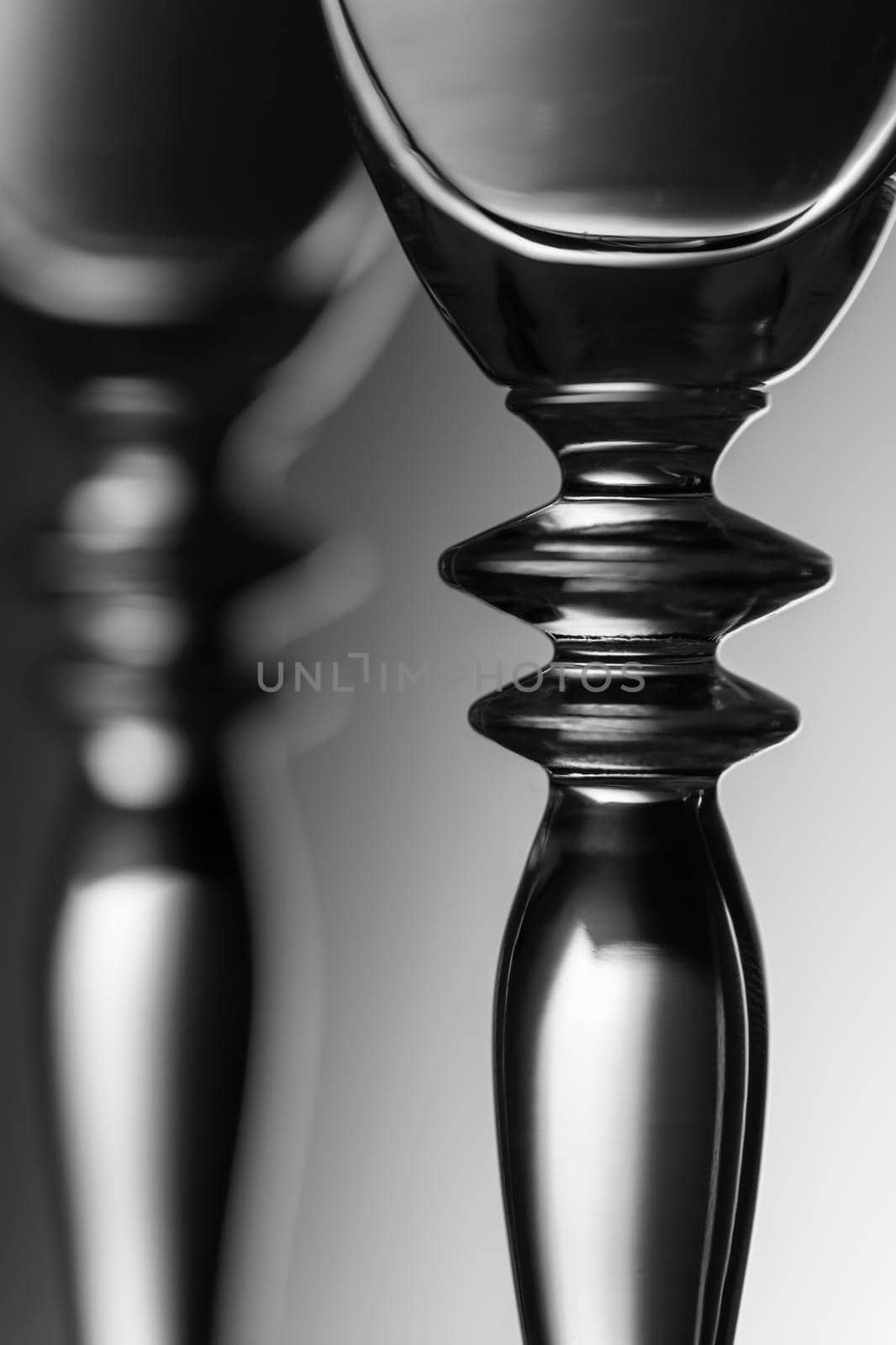 Detailed view of the middle parts of two champagne glasses brightness running background  monochrome. The focus is on the front glass.