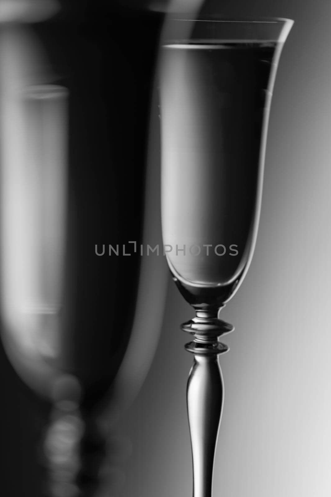 Detailed view of the tops of two champagne glasses against a background with brightness gradient  monochrome. The focus is on the rear glass.