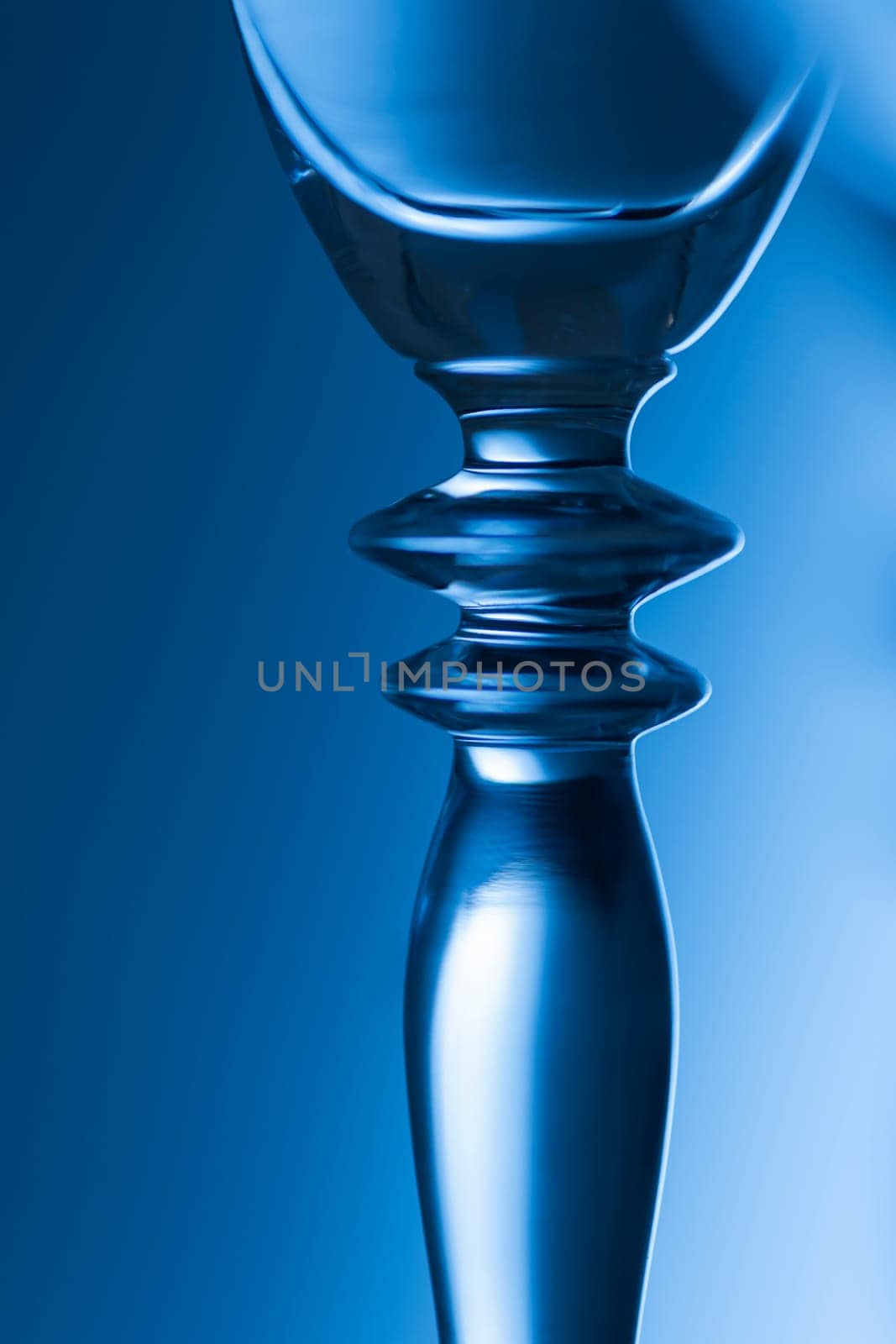 Detailed view of the middle part of a champagne glass with brightness gradient in the background  toned blue.