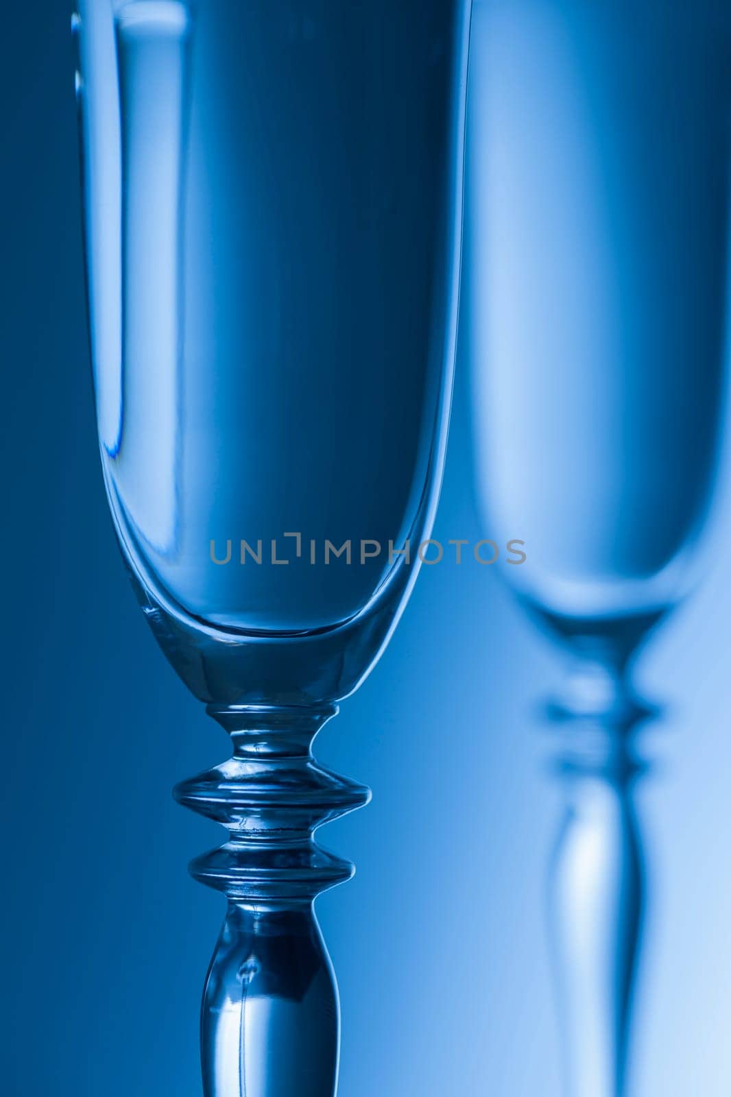 Detailed view of the middle parts of two champagne glasses Brightness running background blue toned. The focus is on the front glass.