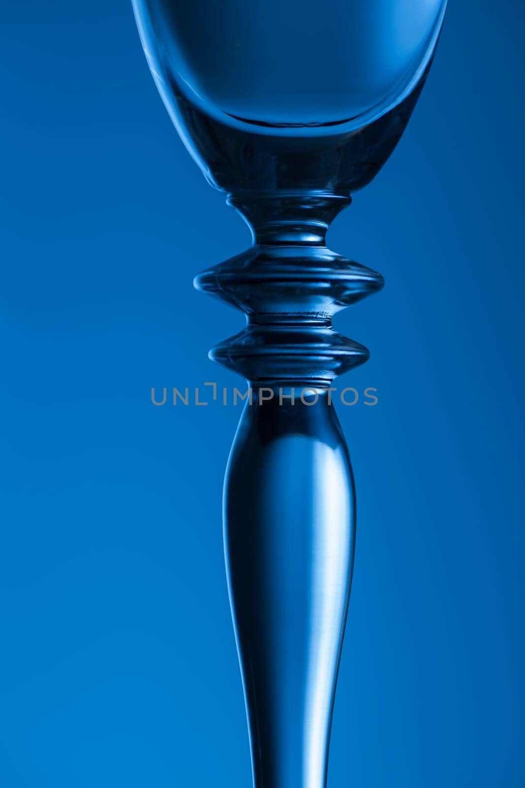 Detailed view of the middle part of a champagne glass with brightness gradient in the background  toned blue.