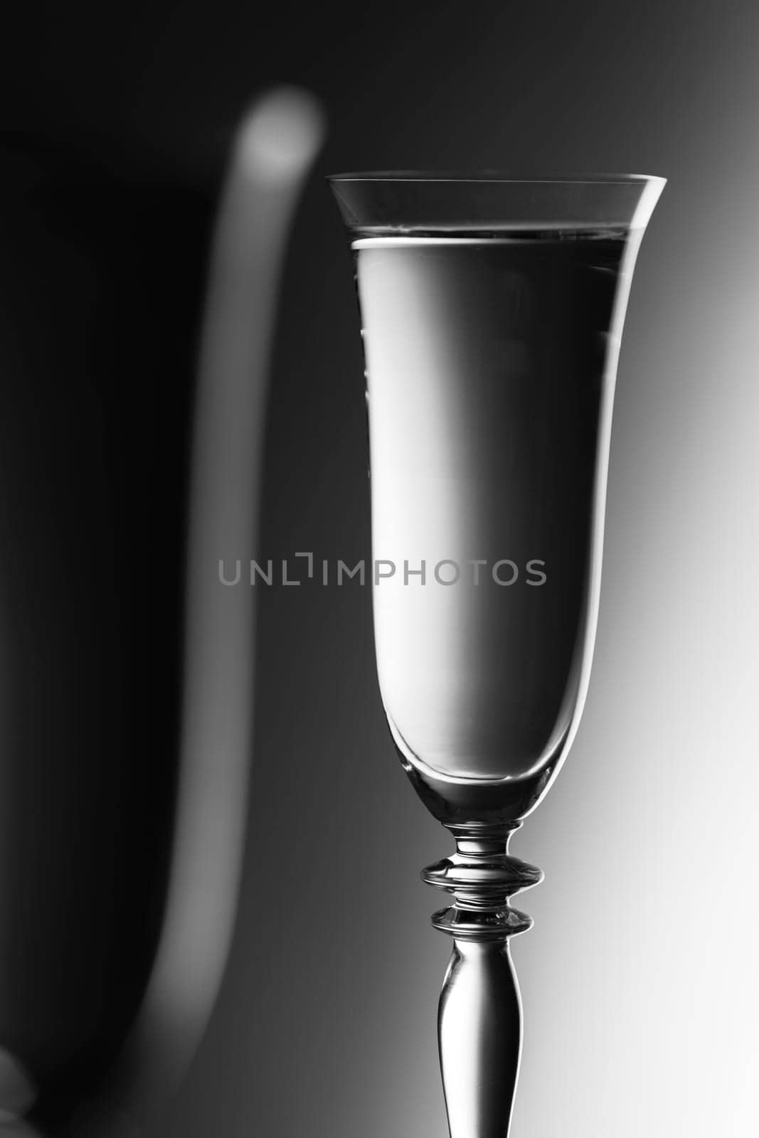 Detailed view of the tops of two champagne glasses against a background with brightness gradient  monochrome. The focus is on the rear glass.