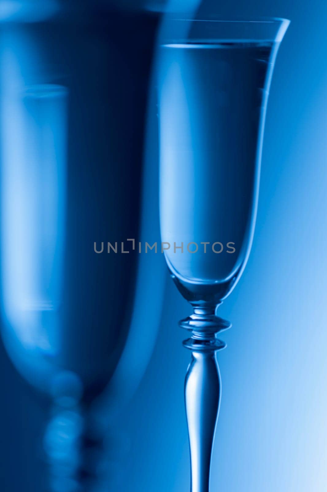 Detailed view of the tops of two champagne glasses against a background with brightness gradient. The focus is on the rear glass.
