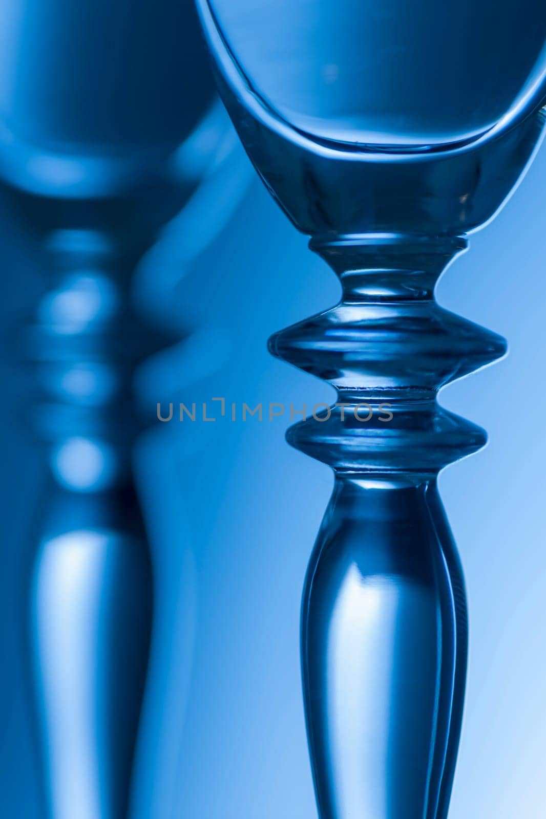 Detailed view of the middle parts of two champagne glasses Brightness running background shaded blue. The focus is on the front glass.