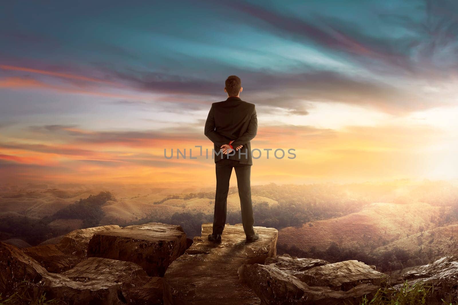 Back view of asian businessman on the top of the hill looking wonderful scenery in mountains during sunset