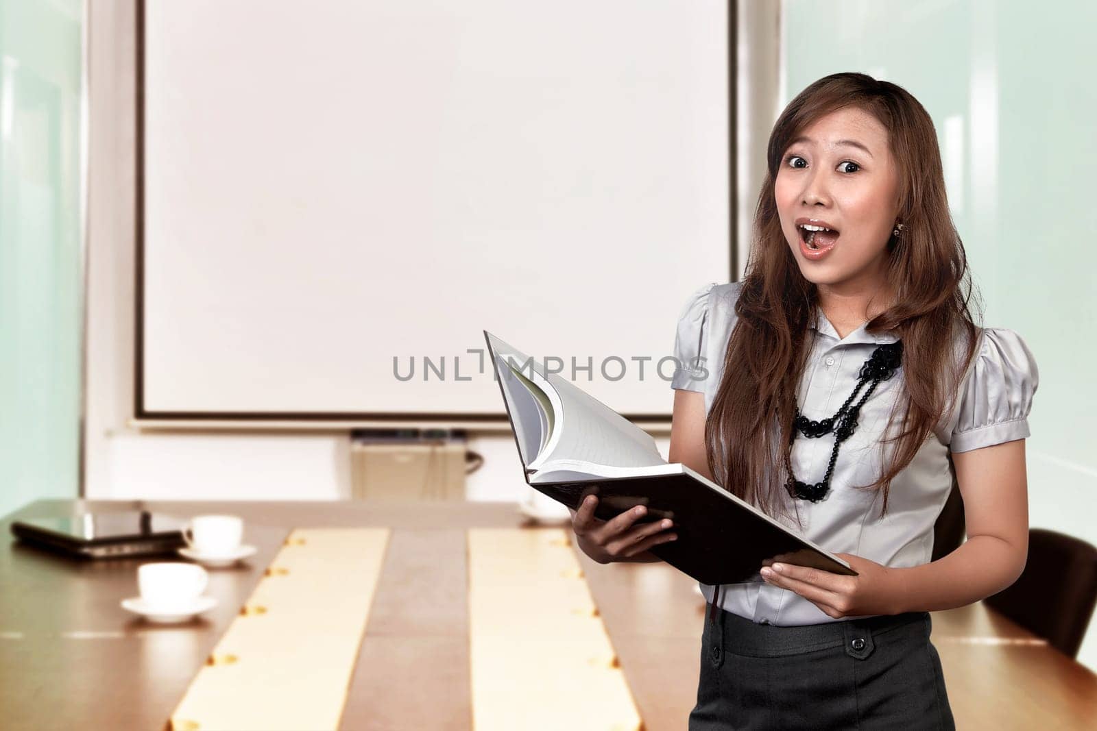 Portrait asian business woman looking surprised while holding document over meeting room at office