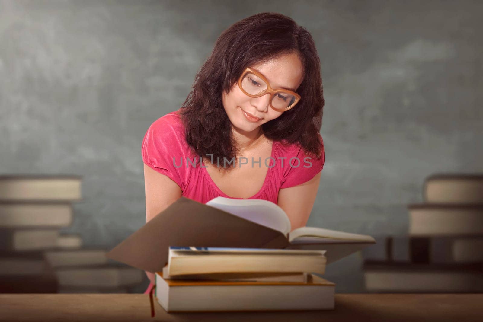 Charming asian woman sitting by wooden table and reading book with stacked book on background
