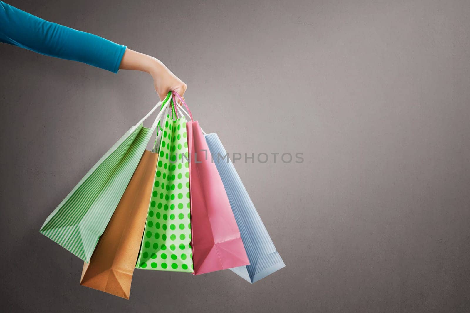 People hand holding colorful shopping bag on grey background