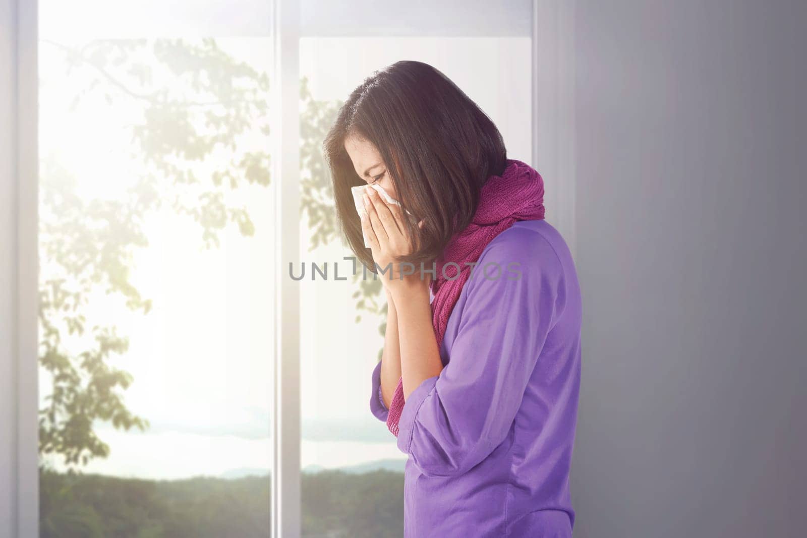 Sick asian woman holding a tissue in her nose at home