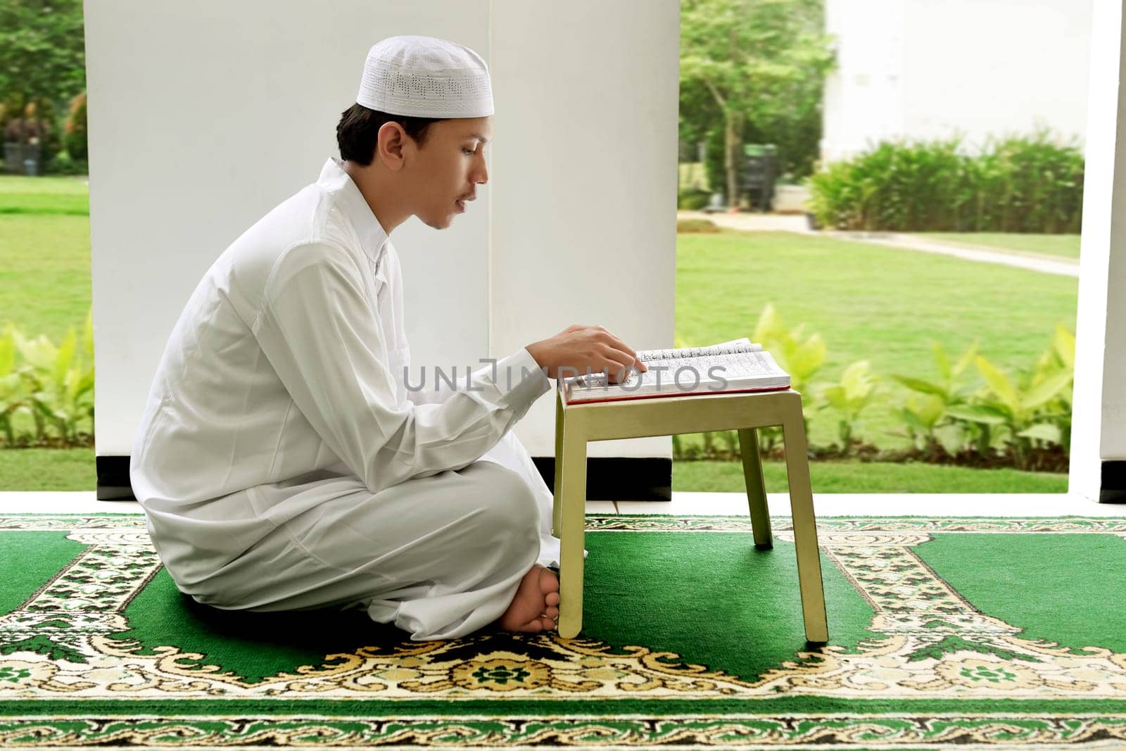 Side view of asian muslim man reading holy book koran on the mosque