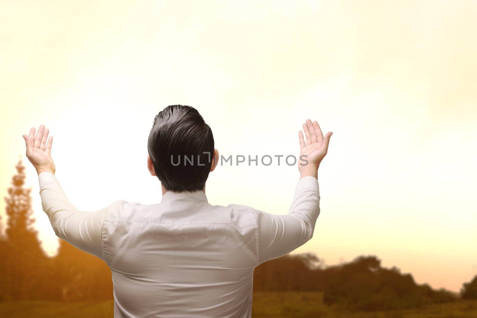 Back view of asian muslim man raising hand and praying during sunset