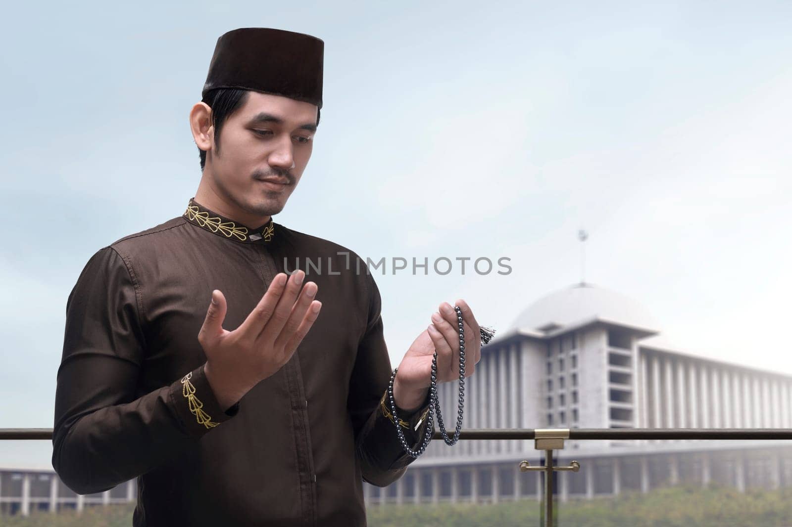 Portrait of asian muslim man raising hand and praying with mosque background