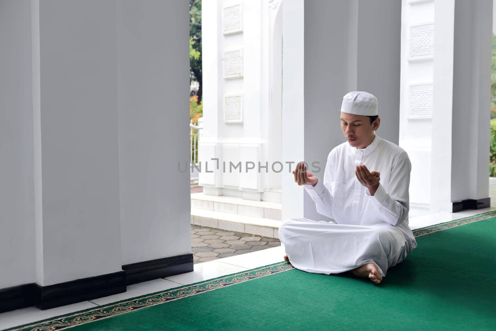 Handsome asian muslim man raising hand and praying on the mosque
