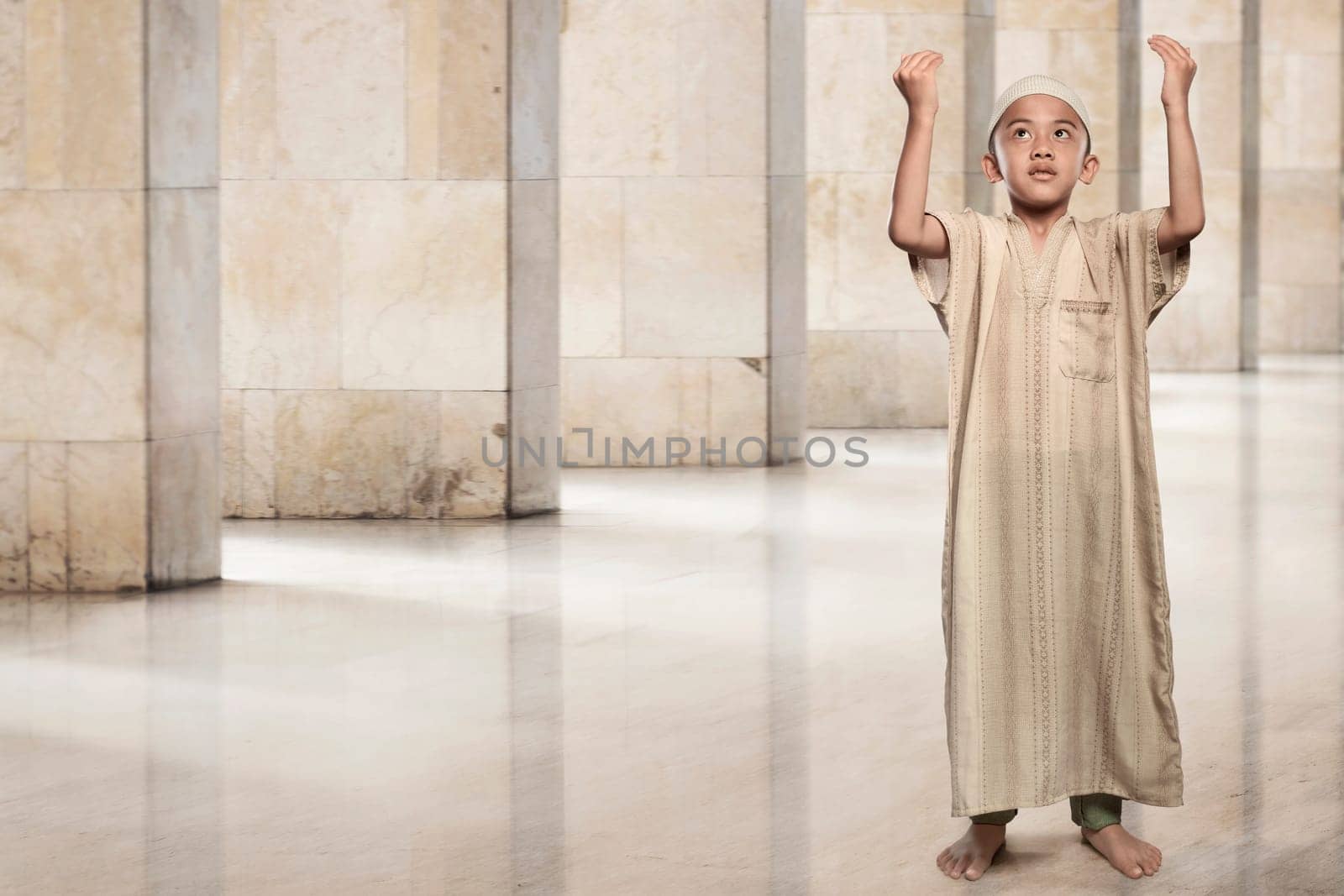 Little asian muslim boy raising hand and praying on the mosque