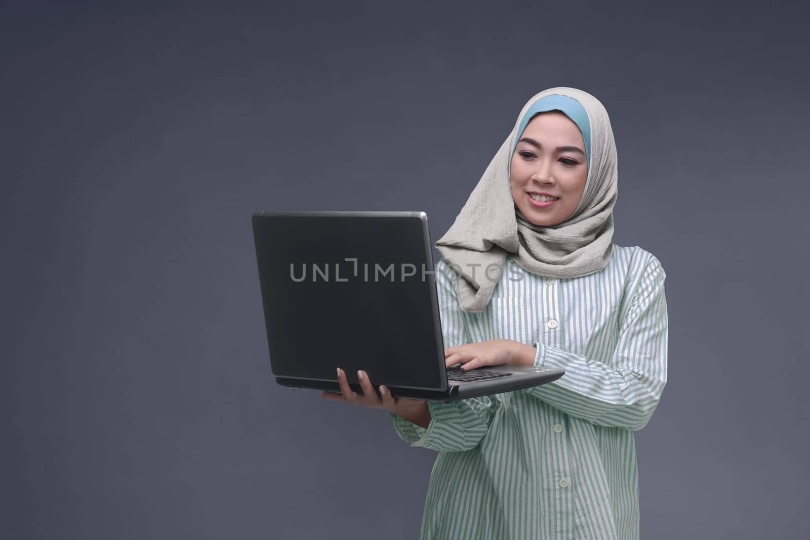Portrit of asian muslim woman with hijab typing on laptop over dark background