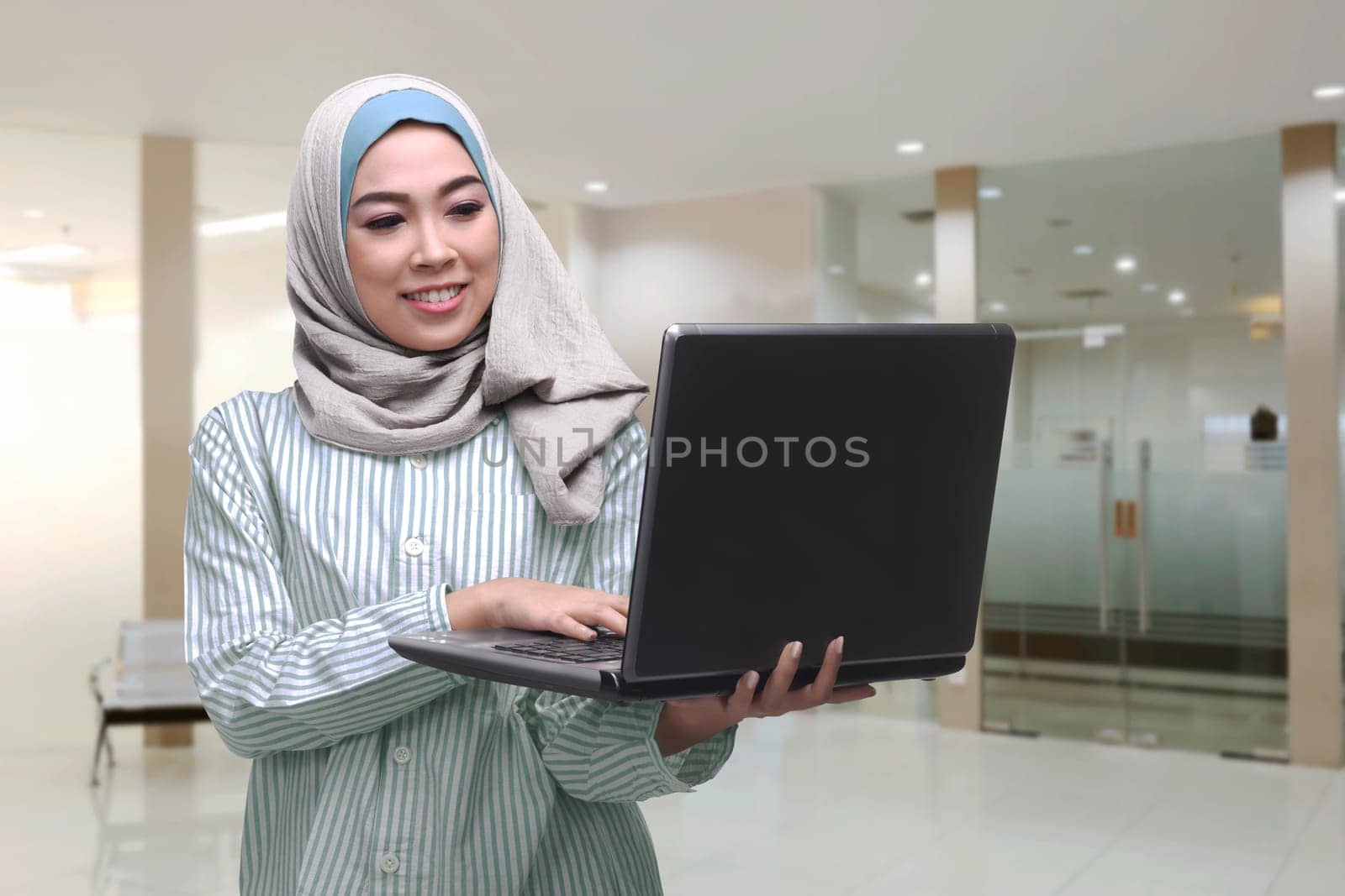 Young asian muslim woman using laptop while standing in the office room