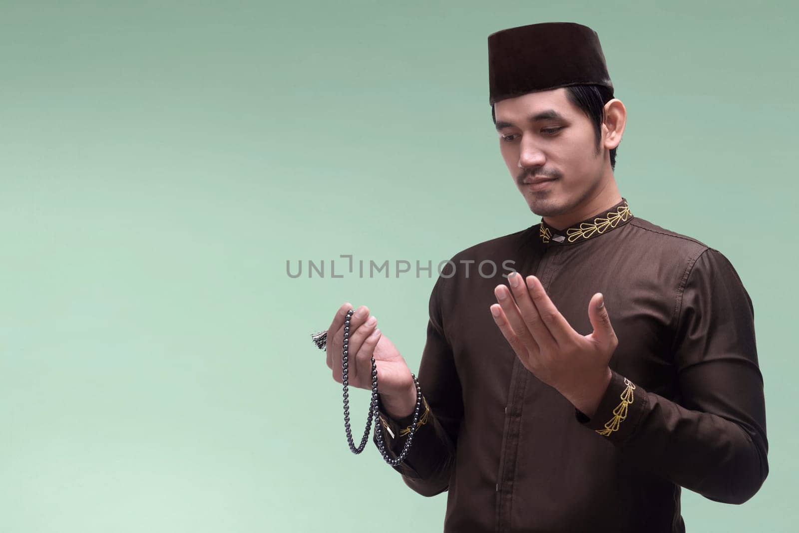Handsome asian muslim man praying to god with prayer beads against bright background
