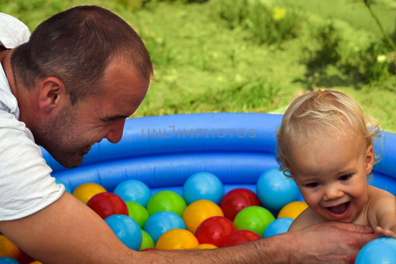 The father and son are playing in small pool with colorful balls.