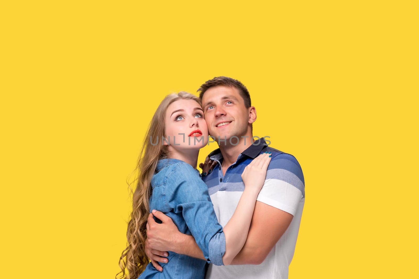 Portrait of a young couple standing against yellow studio background and looking up