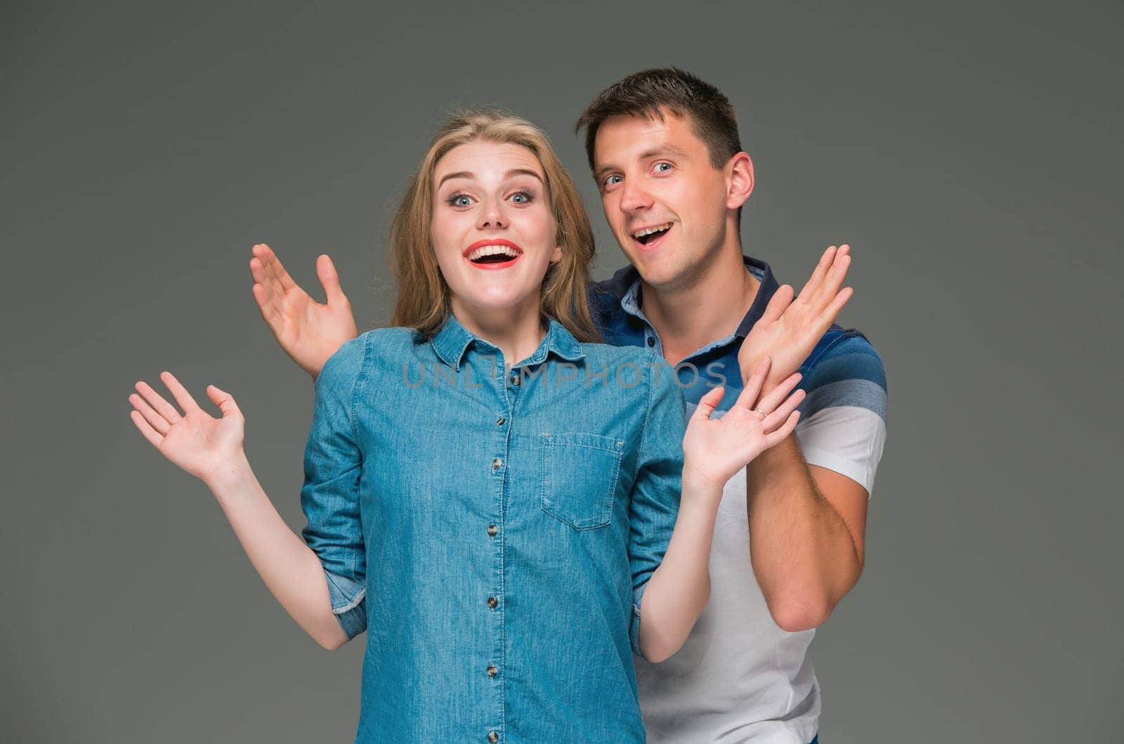 Portrait of a young surprised couple standing against gray studio background