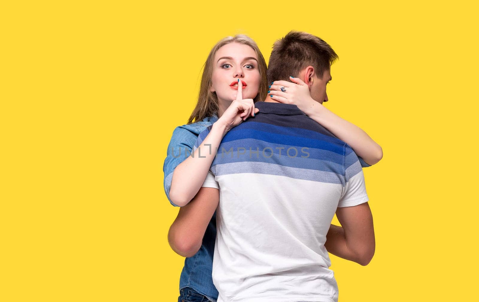 Portrait of a young couple standing against yellow studio background and Calling for silence