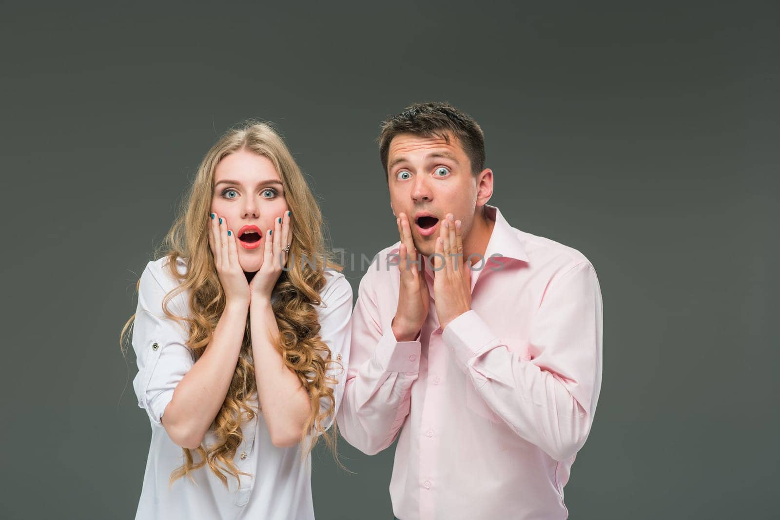 Portrait of a young surprised couple standing against gray studio background