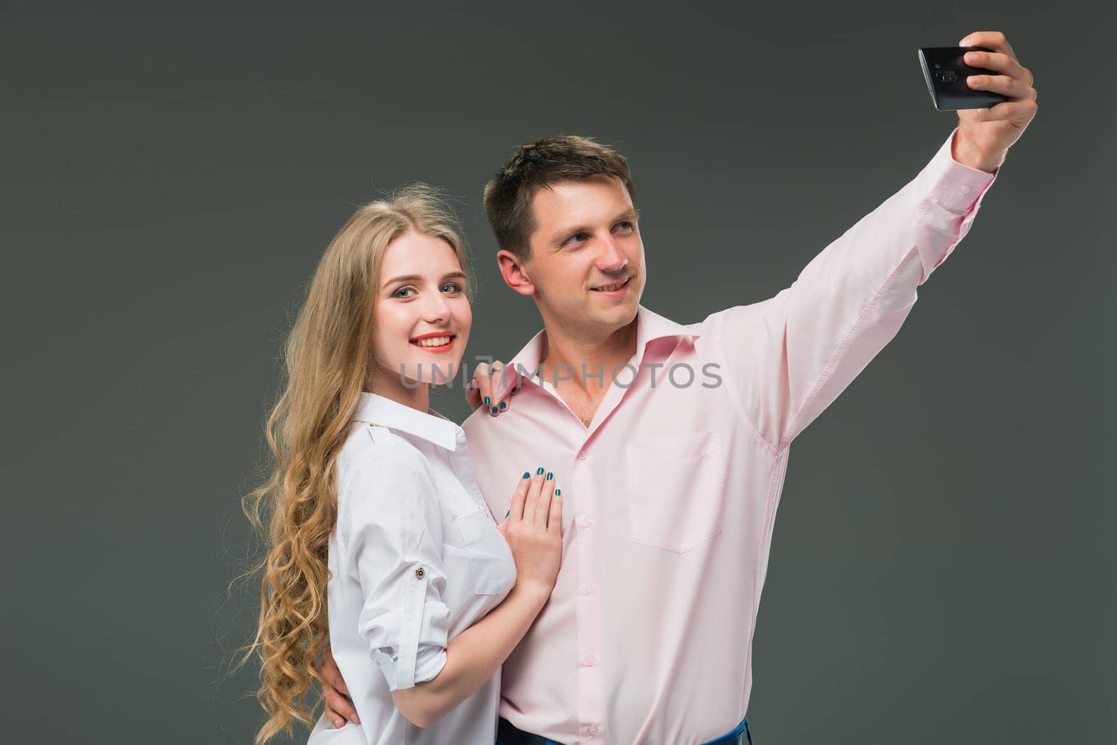 Portrait of a young couple standing against gray studio background and making selfies