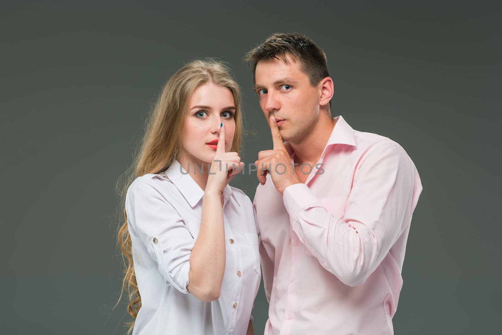 Portrait of a young couple standing against gray studio background and Calling for silence