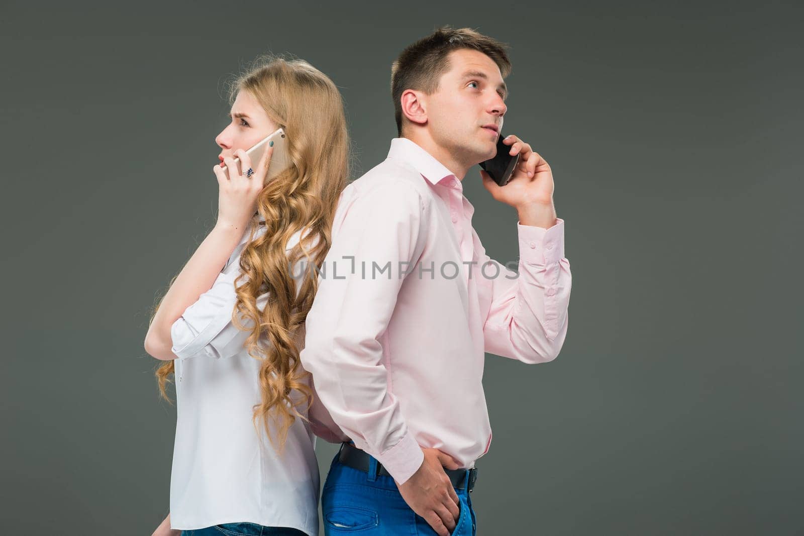 Business concept. The two young colleagues holding mobile phones and speaking on gray studio background