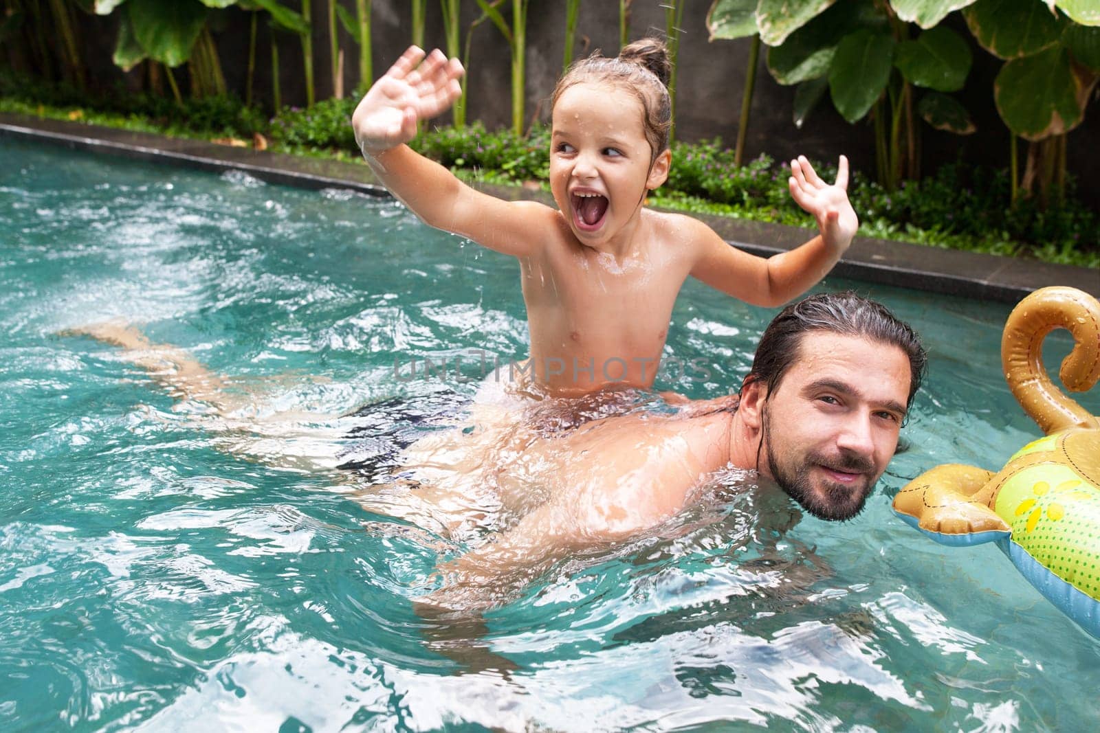 Happy family, active father with little child, adorable toddler girl, having fun together in outdoors swimming pool in water park during sunny summer sea vacation in tropical resort.