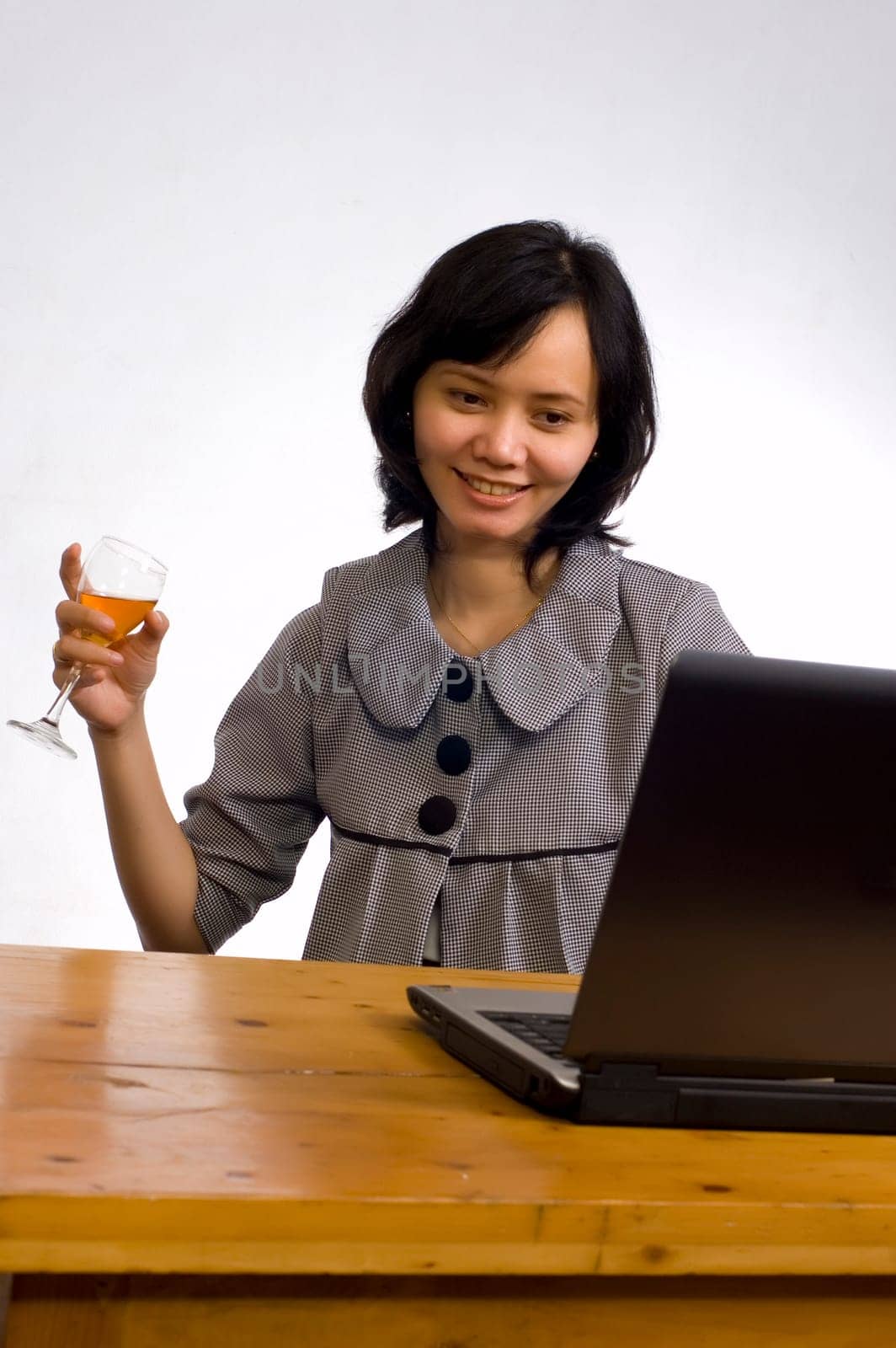 Beautiful asian business woman celebrating her success with wine in front of her computer