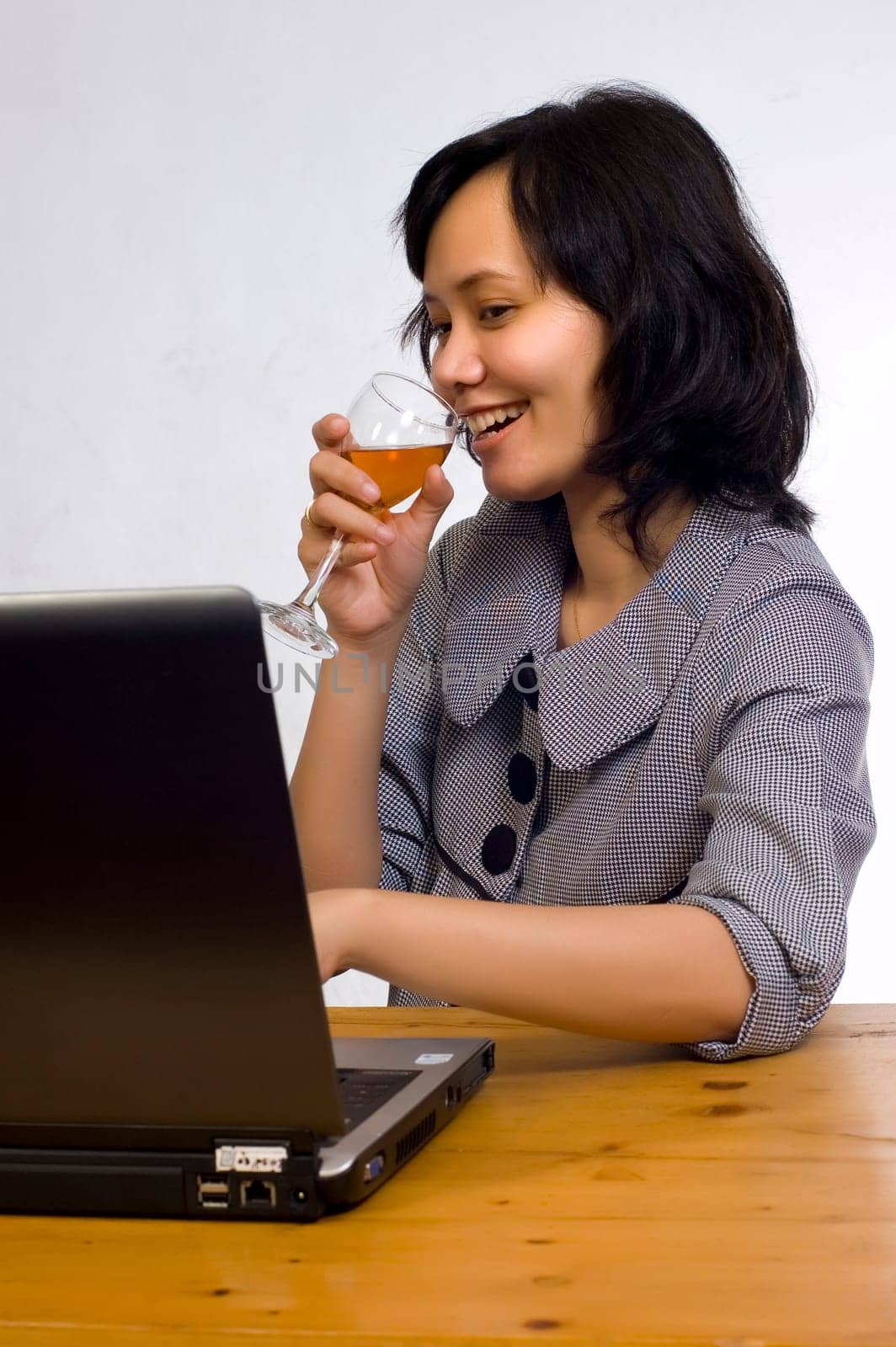 Beautiful asian business woman celebrating her success with wine in front of her computer